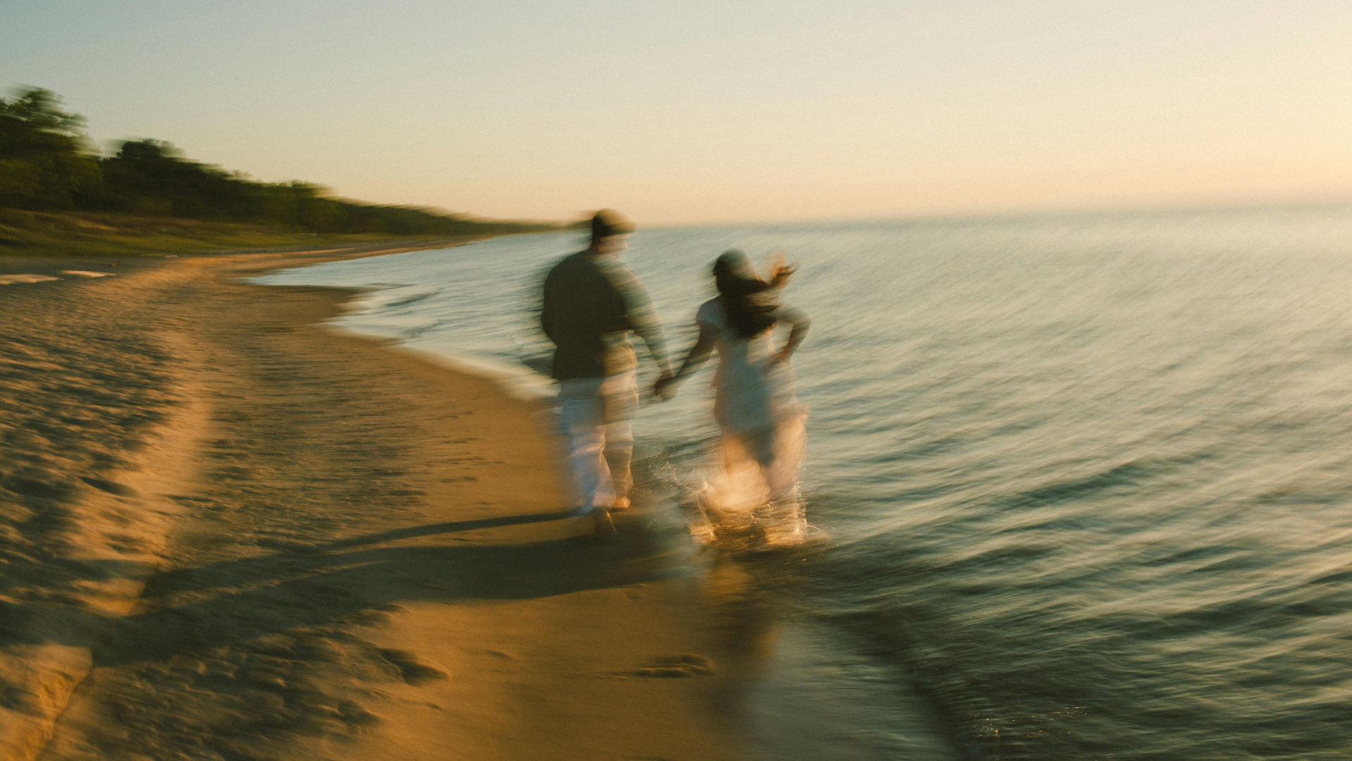 A couple running along the shoreline at sunset